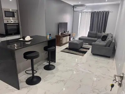 a living room with a couch and a kitchen with stools at Apartamento mais Carro George Mendes in Praia