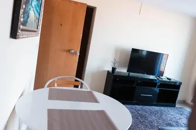 a living room with a tv and a white table and a door at Apartamento T1 em Palmarejo, Trás de pão quente in Praia