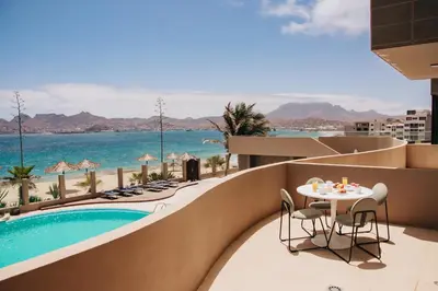 a balcony with a table and chairs and a pool at Pôr D'Sôl Mindelo in Lazareto