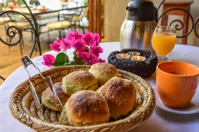 a basket of pastries on a table with orange juice and flowers at The Colonial Guest House in São Filipe