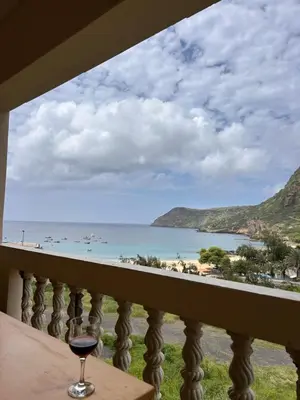 a glass of wine sitting on a balcony looking out at the ocean at Sun & Sea Tarrafal in Tarrafal