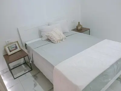 a white bedroom with a large bed and a table at Apartamento Cidade in Mindelo