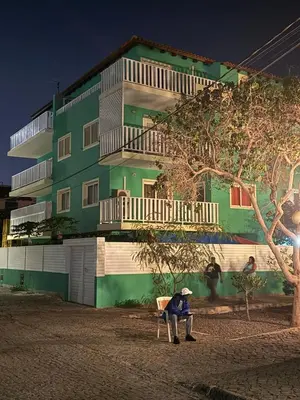 a person sitting on a bench in front of a green building at Estrela Mar - Wi-Fi included in Santa Maria