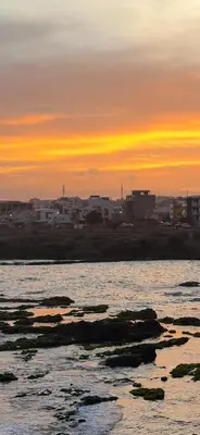 a sunset over the ocean with rocks in the water at Condominio atlantico ll in Praia