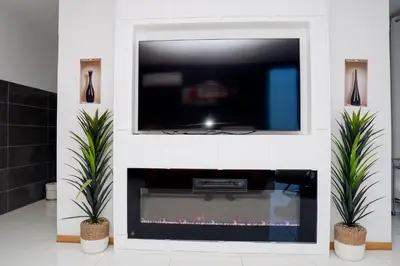 a tv above a fireplace in a living room with two plants at Kretxeu Luxury Villa in Praia