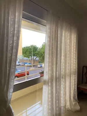 a window with white curtains and a view of a street at Mindelo Family Apartment in Mindelo