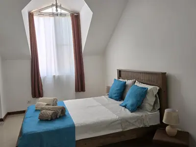 a bedroom with a bed with blue pillows and a window at Diva Apartamento in Praia