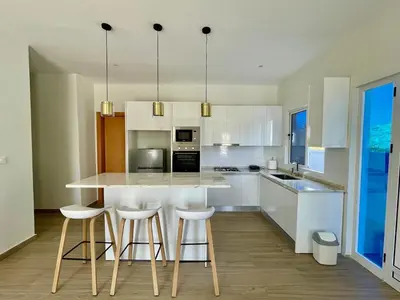 a kitchen with white cabinets and a island with bar stools at Brand New 2-Bedroom Apartment with AC & Fast Wi-Fi in São Filipe