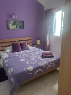a bedroom with a bed with a purple blanket and a window at Maderalzinho in Mindelo