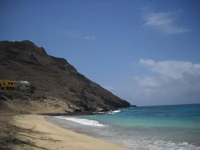 a beach with a hill and the ocean and a house at Pousada B&B Le Gourmet in São Pedro