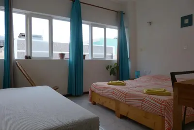 a bedroom with two beds and a window with blue curtains at Casa D'Mar in Ponta do Sol