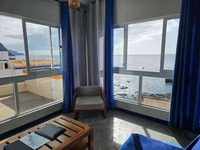 a room with windows and a chair and the ocean at kasa Tambla in Ponta do Sol