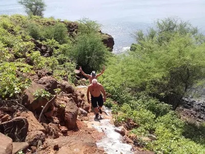 a man walking down a rocky trail with a child on his back at Pousada Villa Concetta AC in Cidade Velha