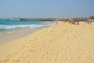 a beach with people sitting on the sand and the ocean at Apartment | in Tropical Resort | pool | close to beach in Santa Maria