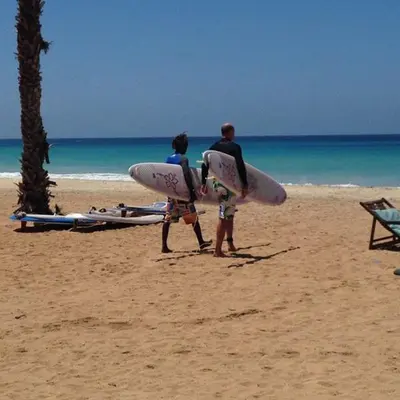 two people walking on the beach with their surfboards at Good value low cost apartment second beach line in Santa Maria