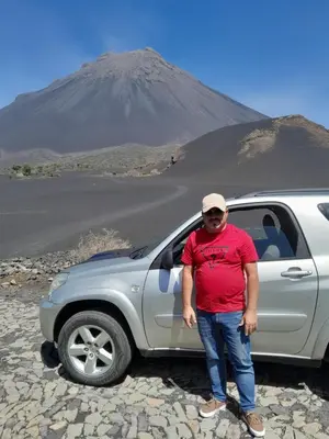 a man standing next to a silver truck in front of a mountain at chez albino guest house in São Filipe