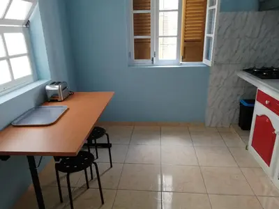 a kitchen with a wooden table and two windows at Résidence Yô in Mindelo