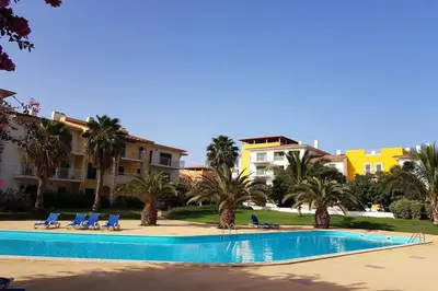 a swimming pool with chairs and palm trees and buildings at Schönes, ruhiges und geräumiges Apartment mit Poolanlage in der Nähe von Santa Maria in Prainha