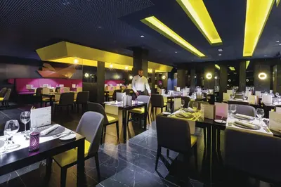 a man standing in a restaurant with tables and chairs at Hotel Riu Funana - All Inclusive in Santa Maria