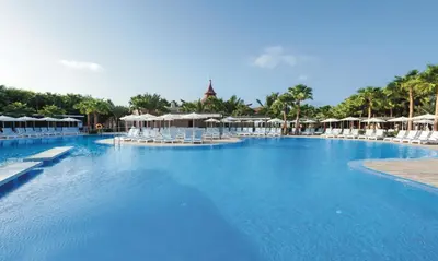 a large swimming pool with white chairs and umbrellas at Hotel Riu Cabo Verde - Adults Only - All Inclusive in Santa Maria