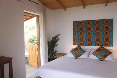 a bedroom with a white bed with a painting on the wall at La Fora Ecolodge in São Filipe