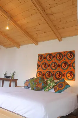 a bedroom with a white bed with a painting on the wall at La Fora Ecolodge in São Filipe