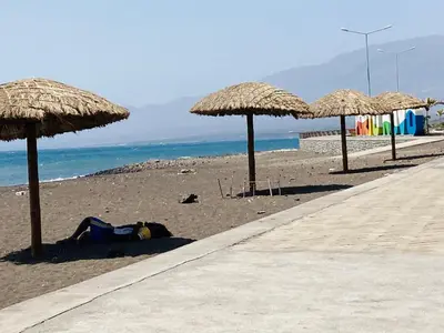 a person laying on the beach under straw umbrellas at Pedra de Rala in Porto Novo