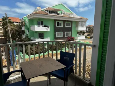 a table and chairs on a balcony with a green house at Leme Bedje - By Bobbywashere in Santa Maria