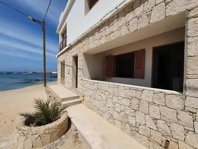 a building with a stone wall next to the beach at Villa Pescadora spectacular view, luxery fisherhouse design in Sal Rei