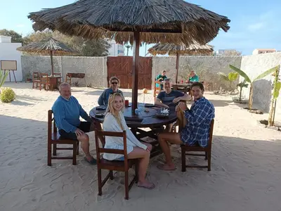 a group of people sitting around a table under an umbrella at Vilas na areia aparthotel in Sal Rei