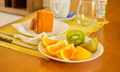 a plate of fruit on a table with a piece of cake at Praia Capital Residence Aparthotel in Praia