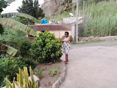 a woman standing next to a bush in front of a house at Pousada Rural Simpatia in Caculi