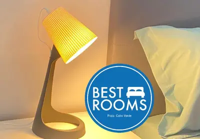 a best rooms sign next to a bed and a lamp at Best Rooms - Quarto 3 Plateau in Praia