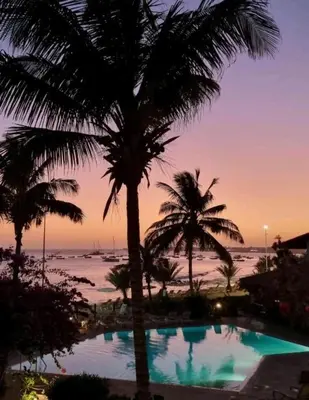 a pool with palm trees and the ocean at sunset at Beach front ocean view Porto Antigo2 Santa Maria in Santa Maria