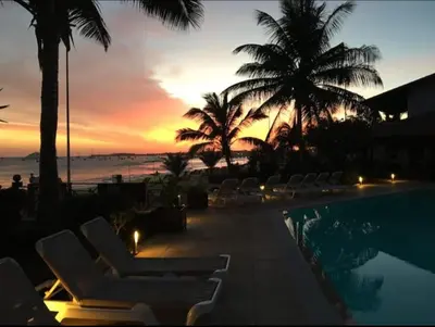a sunset over a swimming pool with chairs and palm trees at Beach front ocean view Porto Antigo2 Santa Maria in Santa Maria