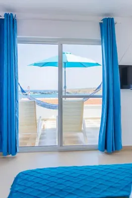 a window with blue curtains and a view of the beach at Sea View Big Lanche in Praia Baixo