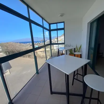 a white table and chairs in a room with a large window at Recanto Verde Cara in Mindelo
