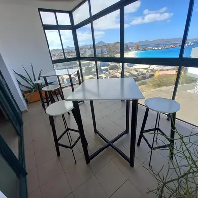 a white table and two stools in a room with a window at Recanto Verde Cara in Mindelo