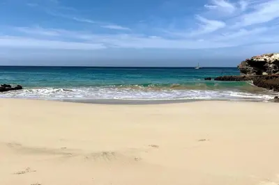 a beach with the ocean and a boat in the water at Villa GÊMEO vue mer, piscine accès privé plage in Calheta Do Maio