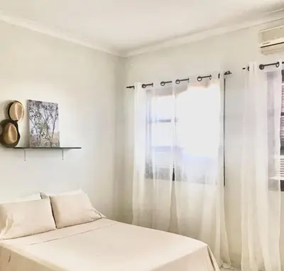 a white bedroom with a bed and a window at Syds Beach House in Praia