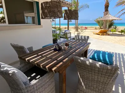 a wooden table and chairs on a patio with the beach at Vila Mare - Praia de Chaves frontline in Cabeçadas