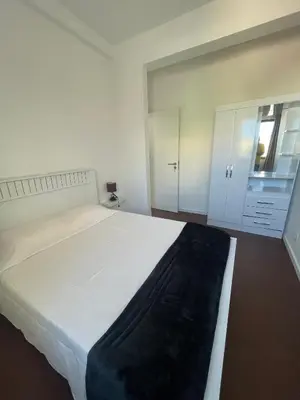 a white bedroom with a large bed and a cabinet at Tia Nita Apartamentos in Mindelo