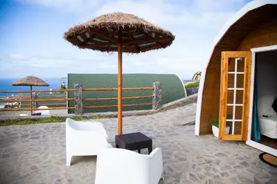 a patio with an umbrella and some white chairs at RM Green Hotel in Lombo Branco