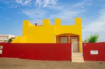 a yellow house sitting behind a red fence at Cosy & Relax Yellow House 5mn walk from the beach! in Calheta Do Maio
