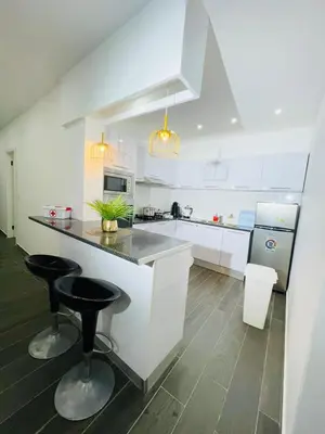 a white kitchen with two bar stools and a counter at Résidence Cazino Apartamentos in Praia